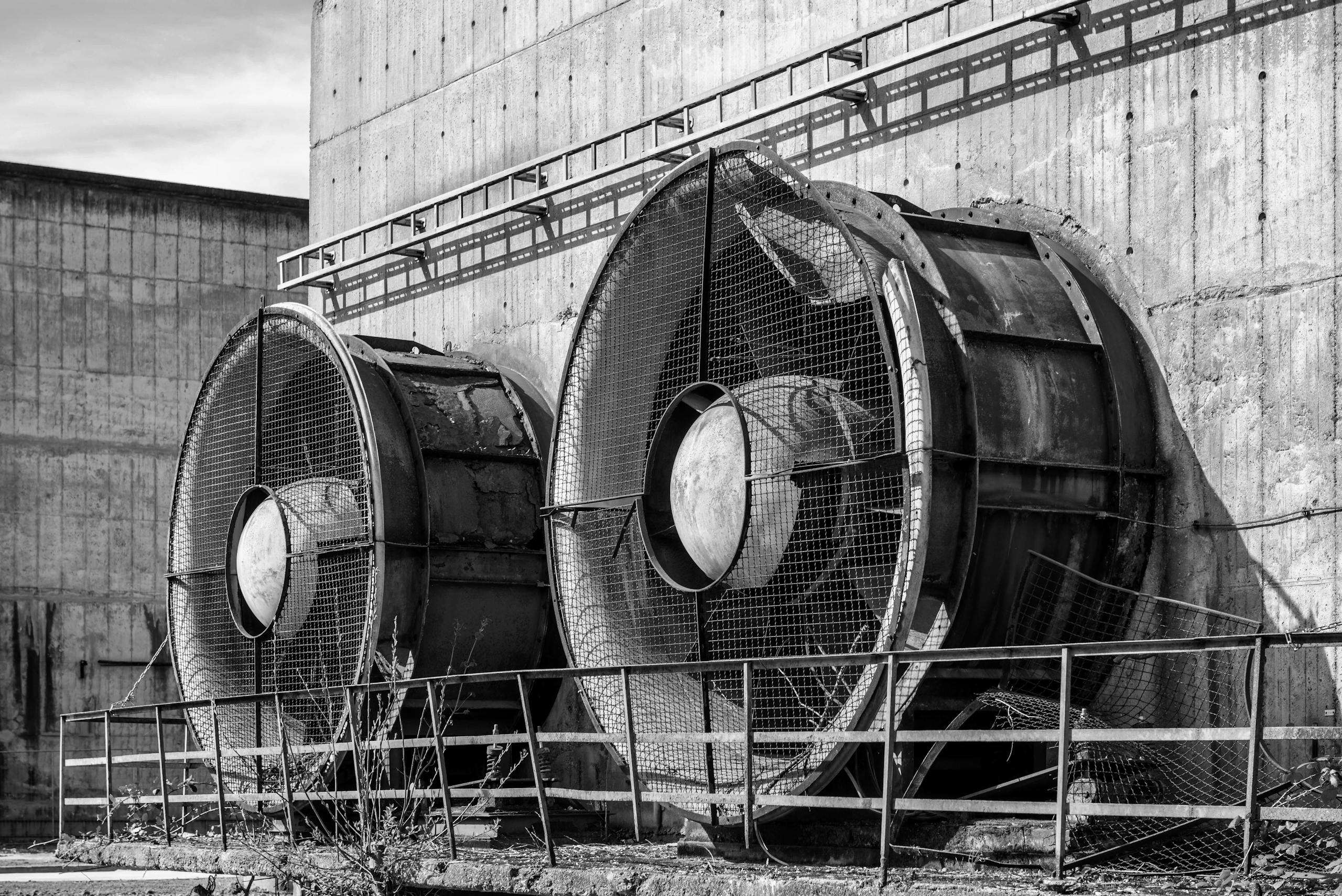 Black and white photo of industrial fans mounted on a concrete wall in an urban environment.