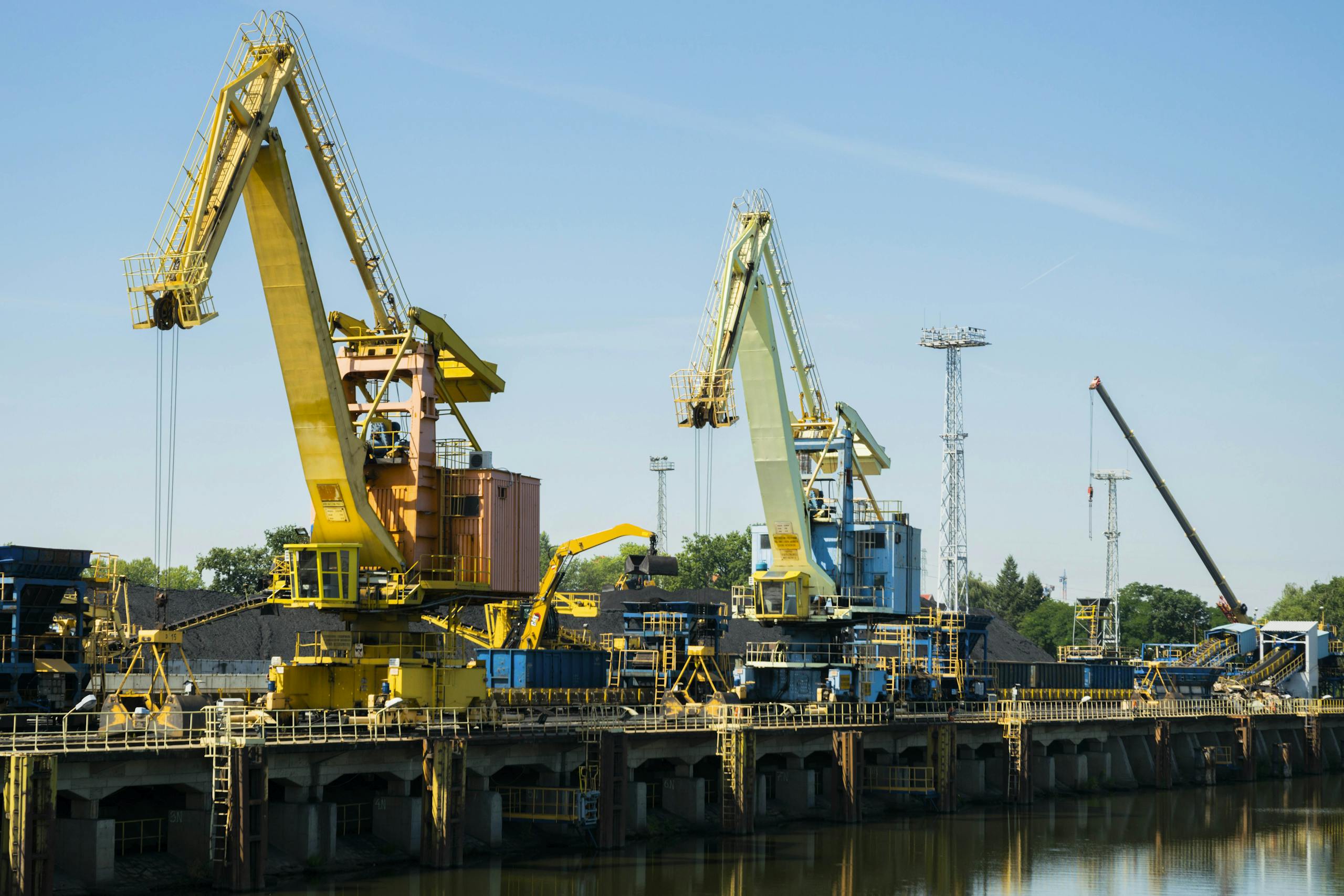 Large industrial cranes are positioned at Wrocław's Odra River port under a clear sky.
