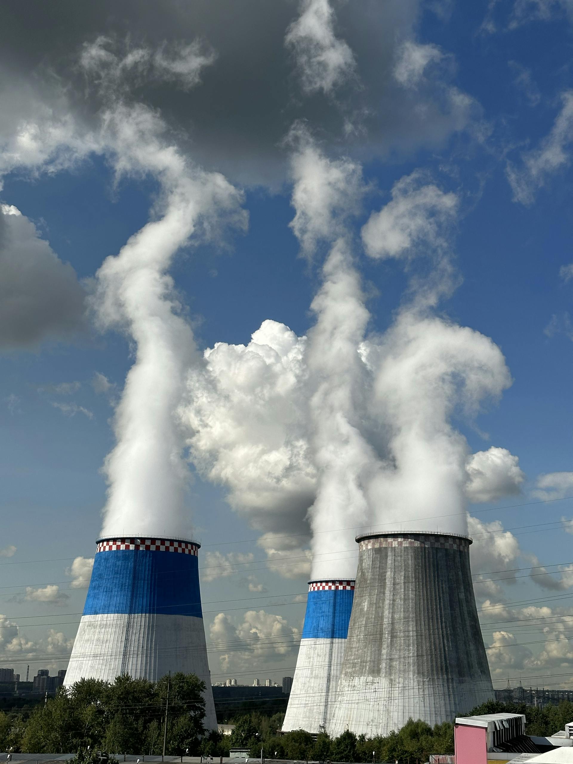 Three industrial cooling towers releasing steam under a bright blue sky.